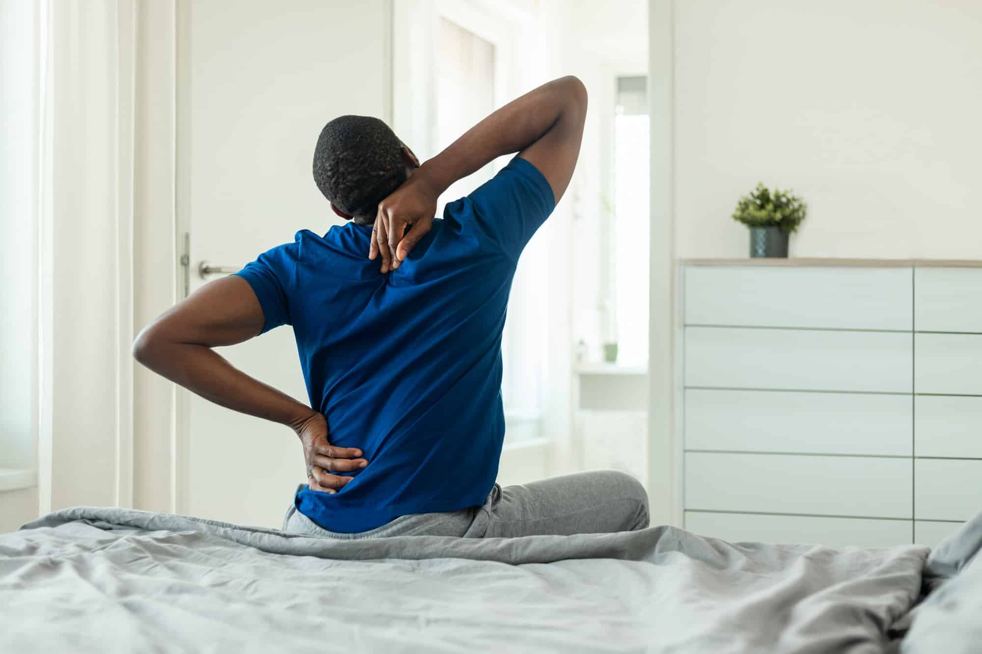 African Man Touching Aching Neck And Spine Sitting In Bedroom